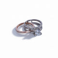 Two rings, one rose gold and one silver with a diamond, on a light gray background.