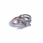 Two rings, one rose gold and one silver with a diamond, on a light gray background.