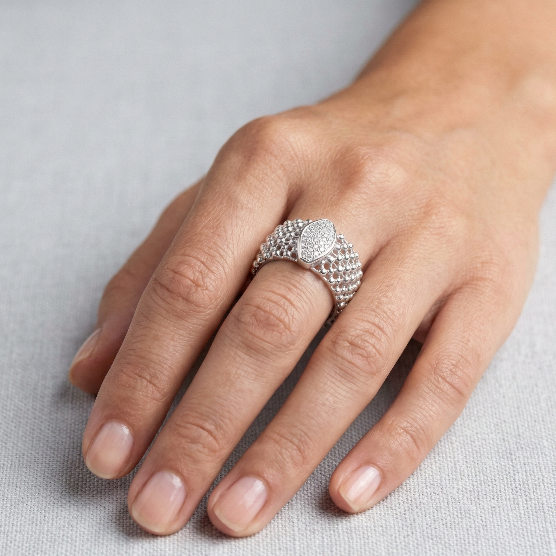 Hand wearing a silver ring with a textured band and clear stones on a light gray background