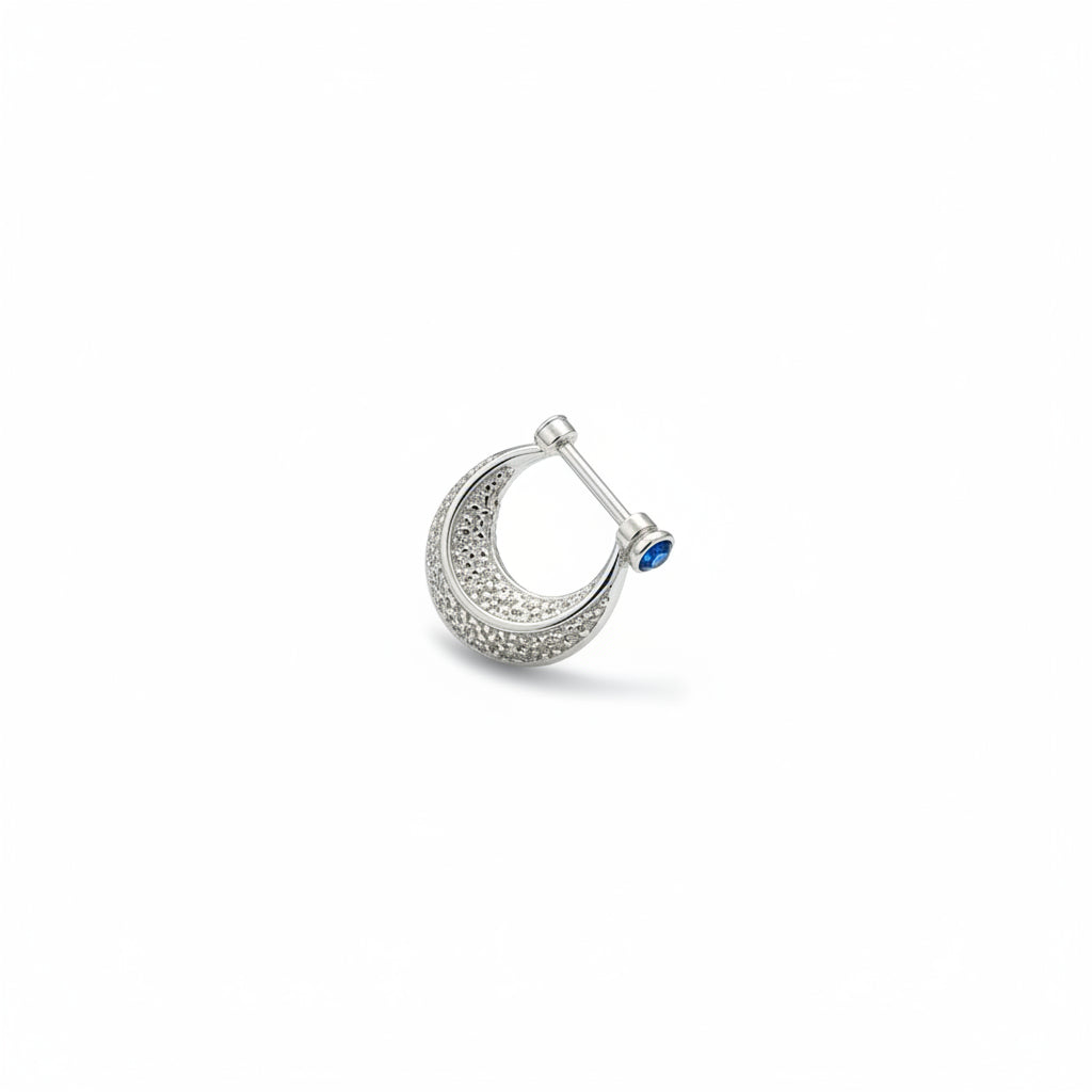 Close-up of a hand holding a silver ring with a blue stone against a blurred background.