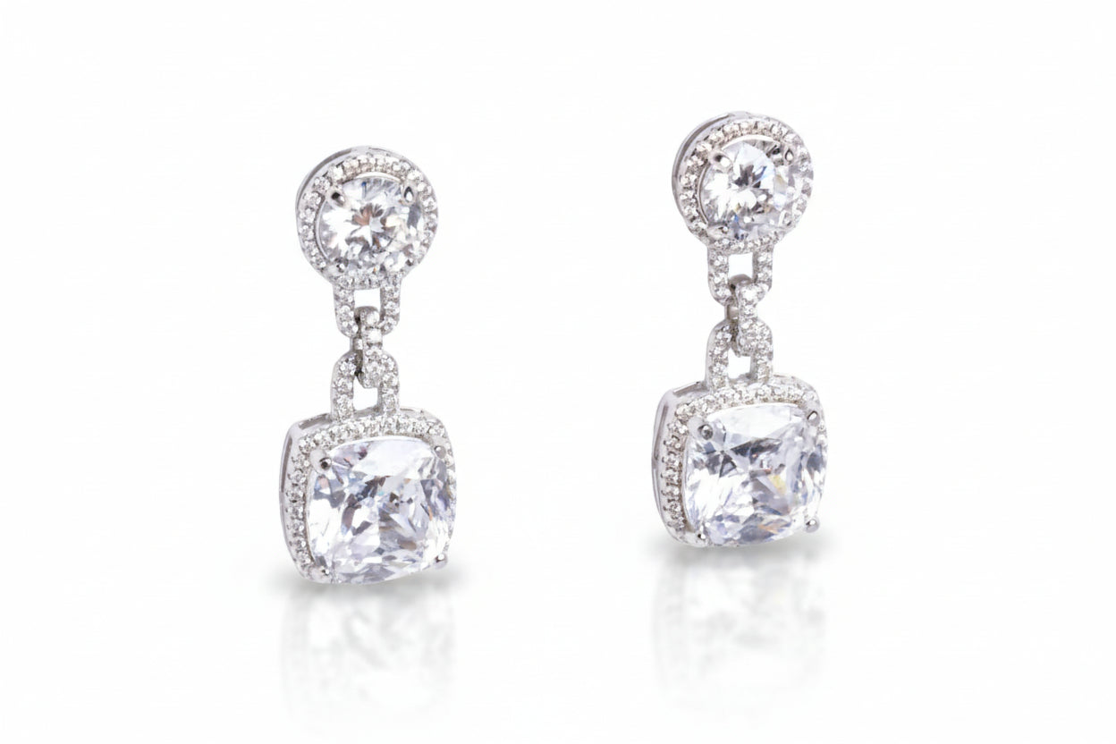 Pair of silver earrings with clear gemstones on a light gray background