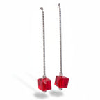 Pair of earrings with red cube-shaped beads on silver chains against a white background