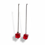 Pair of earrings with red cube beads on silver chains against a white background