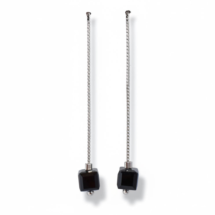 Pair of earrings with black square beads and chain extensions on a light gray background