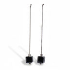 Pair of earrings with black square beads on silver chains against a white background
