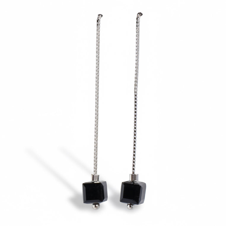 Pair of earrings with black square beads on silver chains against a white background