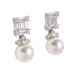Pair of pearl earrings with diamond-like stones on a light gray background